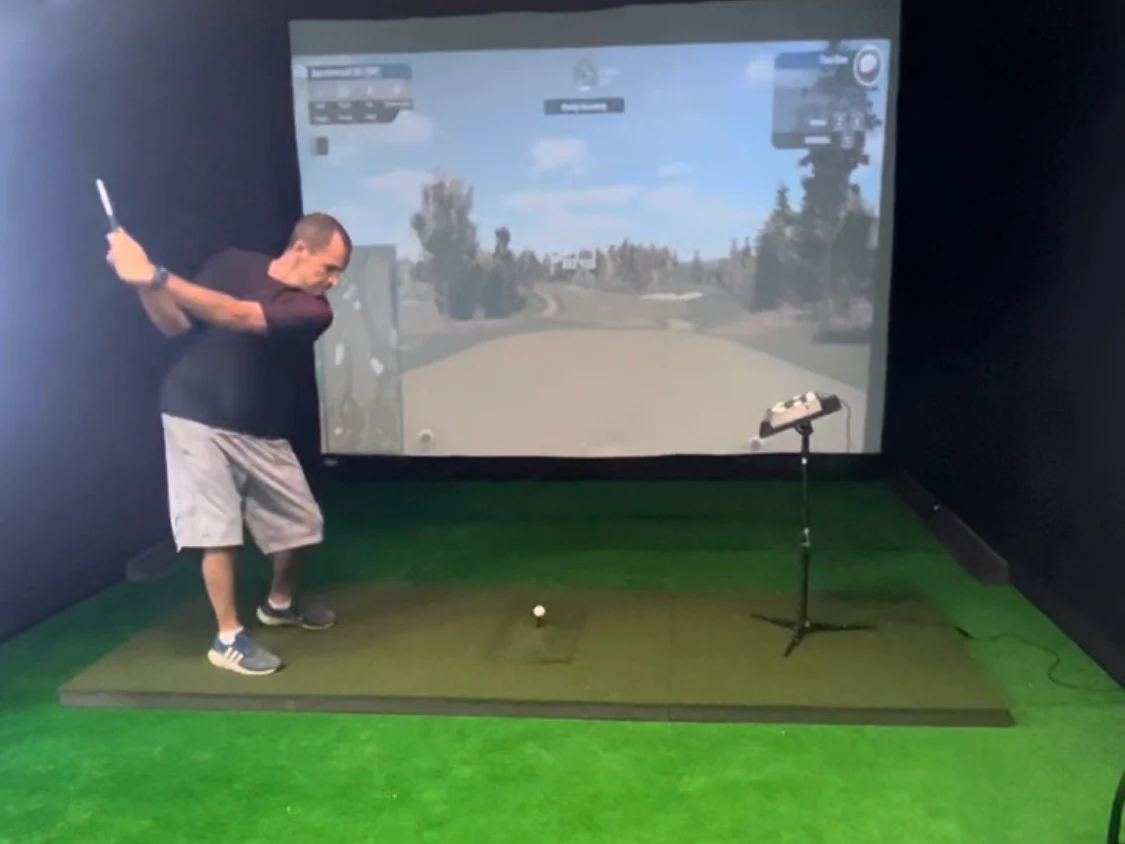 Golfer mid-swing in a simulator bay